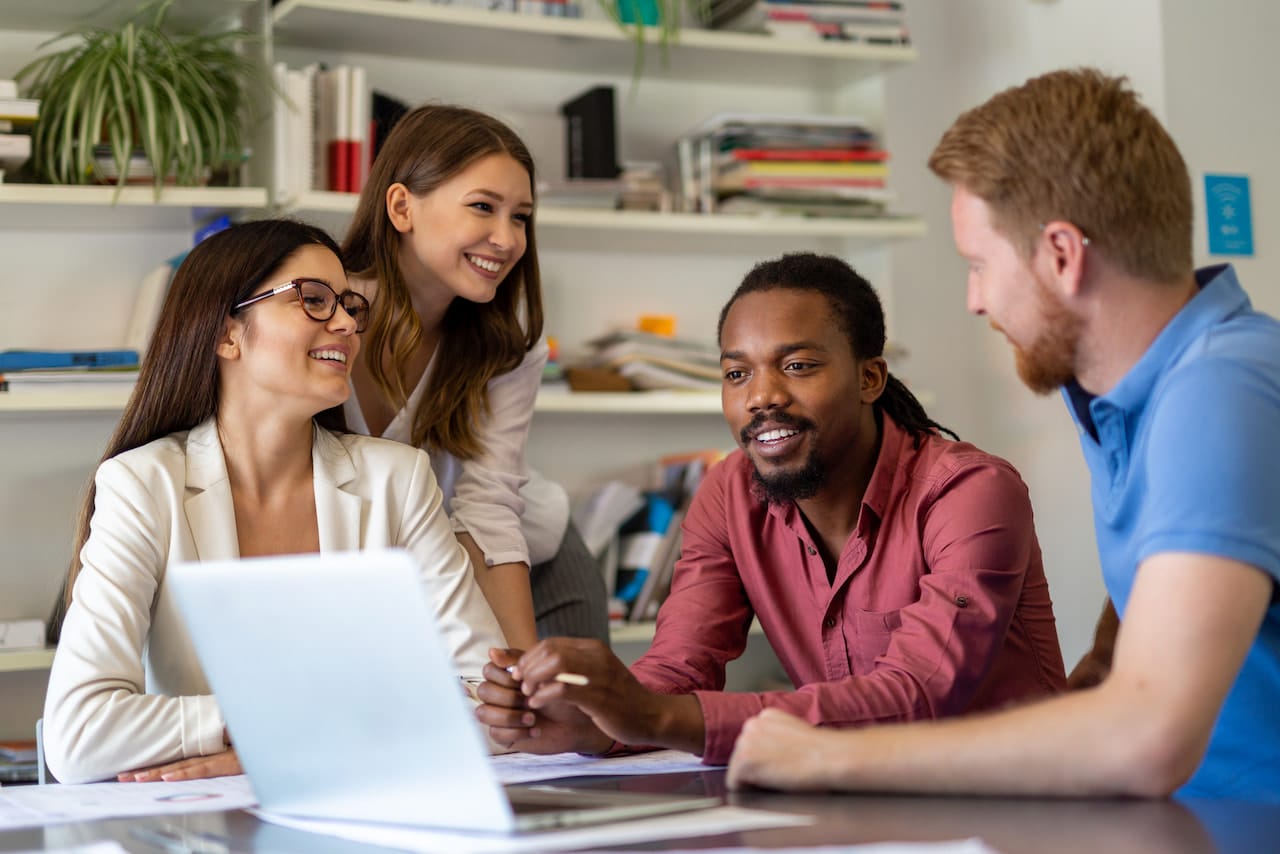 Four business employees engaged in a discussion around a laptop in an office setting.