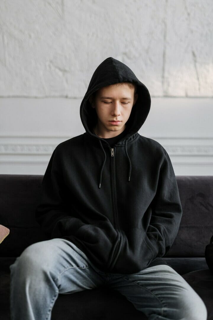 A student in a black hoodie and jeans sitting on a couch with closed eyes, reflecting on their mental health.